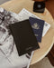 Black passport holder with a passport and boarding pass on a wooden table.